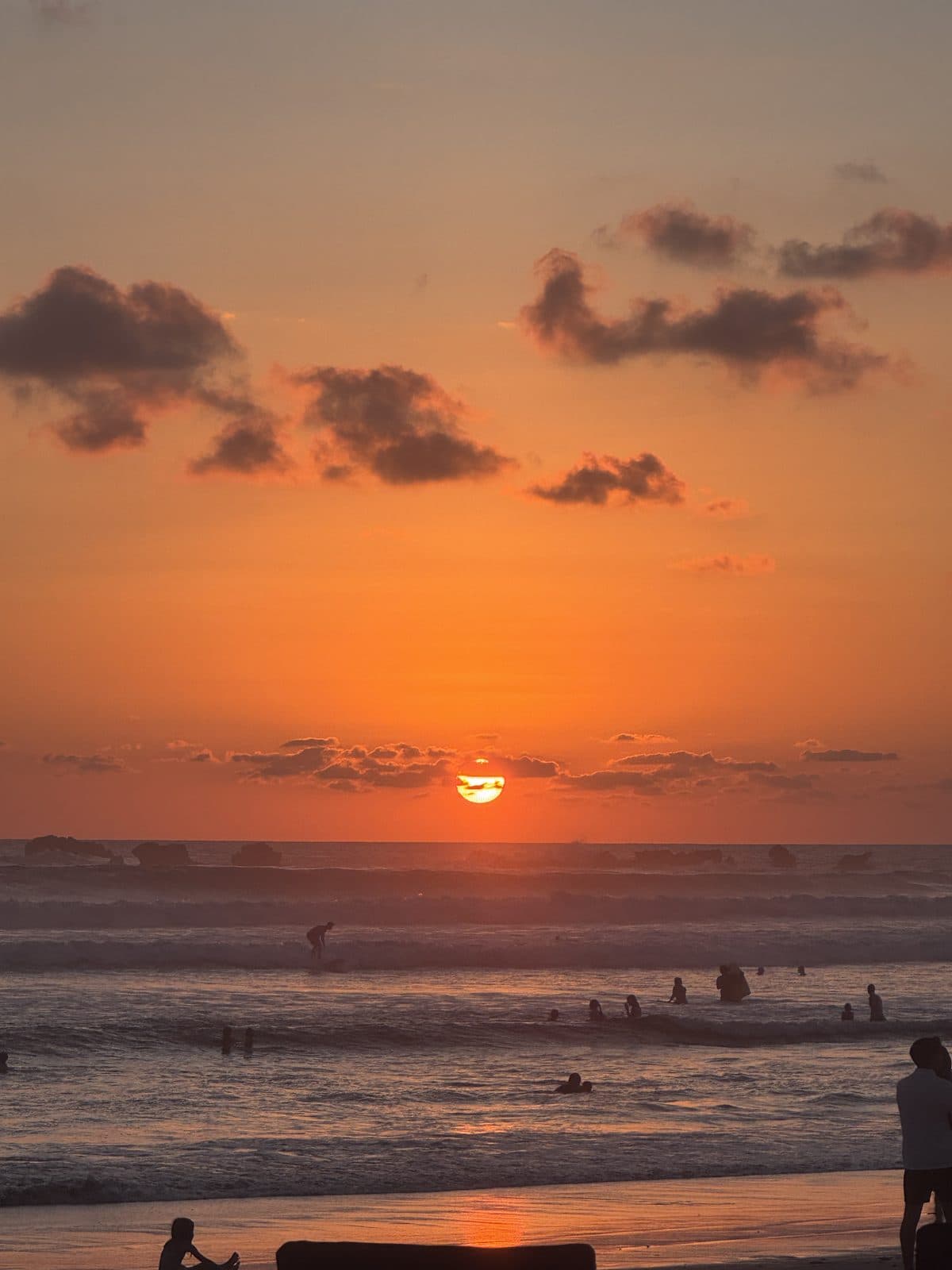 Dos personas conversando al atardecer en Playa Guiones, una con licra de Dispatch